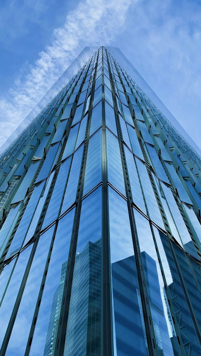 low-angle photography of blue glass walled high-rise building under blue and white sky